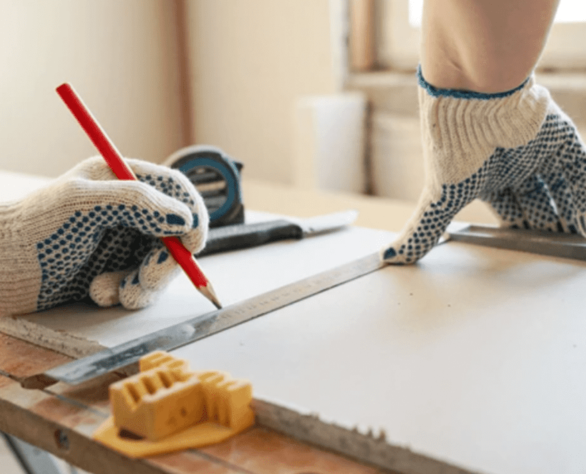 Worker measuring drywall at a construction site.